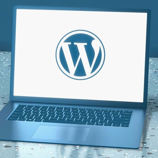 A laptop on a terrazzo surface displays the WordPress logo on its screen against a plain white background.