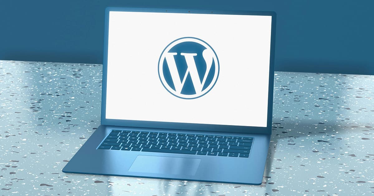 A laptop on a terrazzo surface displays the WordPress logo on its screen against a plain white background.